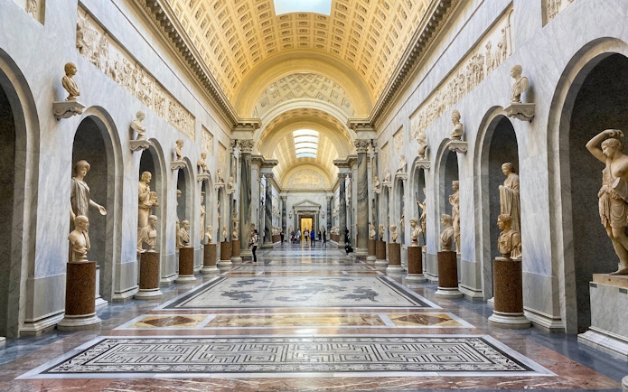 Vatican Museums gallery with classical statues and ornate ceiling.