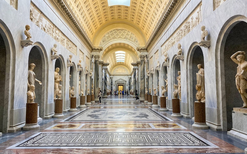 Vatican Museums gallery with classical statues and ornate ceiling.