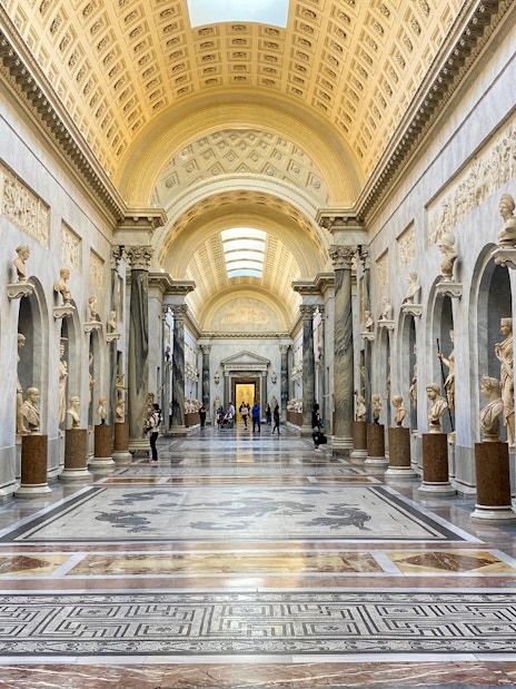 Vatican Museums gallery with classical statues and ornate ceiling.
