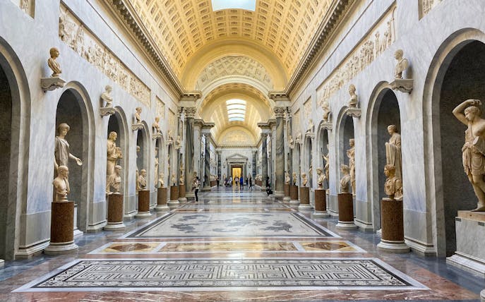 Vatican Museums gallery with classical statues and ornate ceiling.