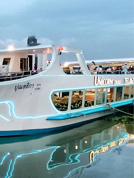 Unicorn Dinner Cruise boat docked in Bangkok with city skyline in the background.