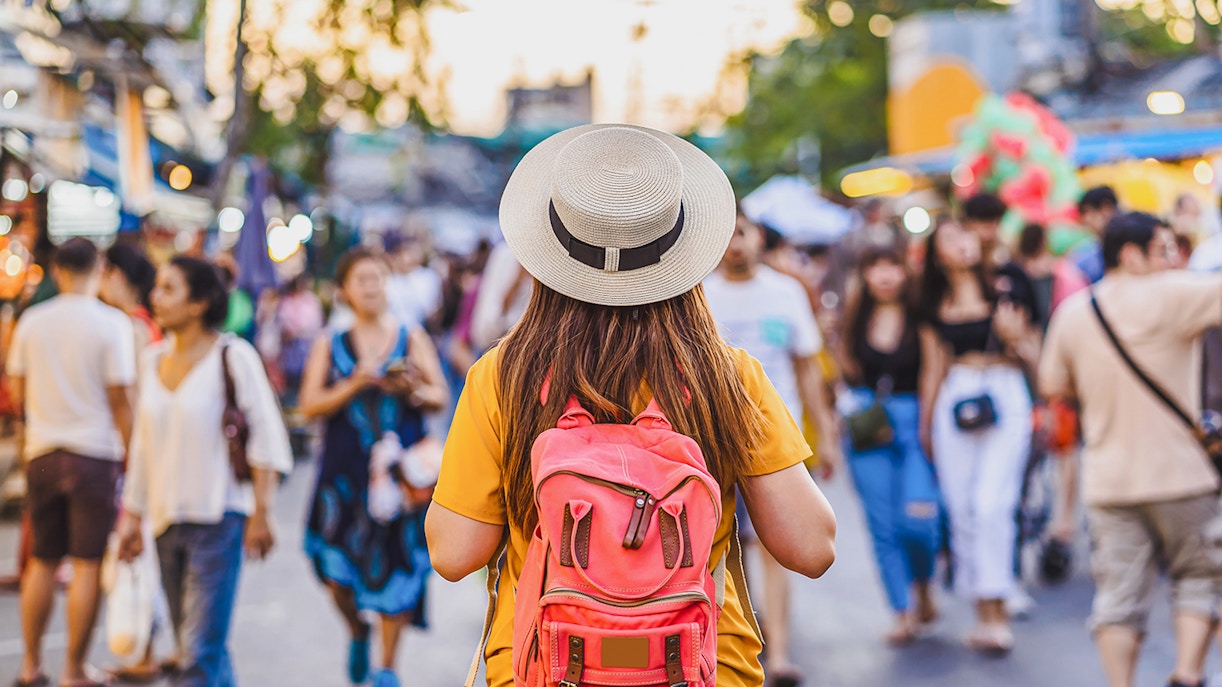 Tourist with backpack exploring a busy street market in Bangkok.
