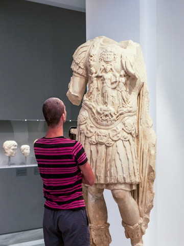 Tourist viewing ancient statue at Heraklion Archaeological Museum, Crete, Greece.