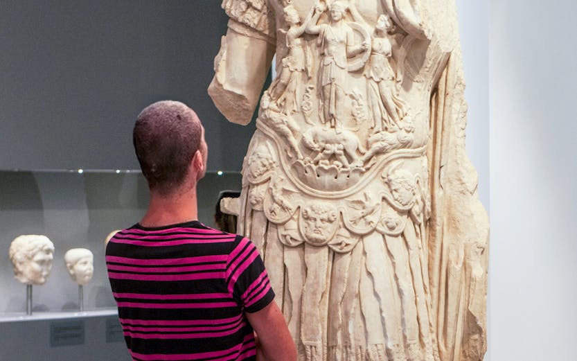 Tourist viewing ancient statue at Heraklion Archaeological Museum, Crete, Greece.