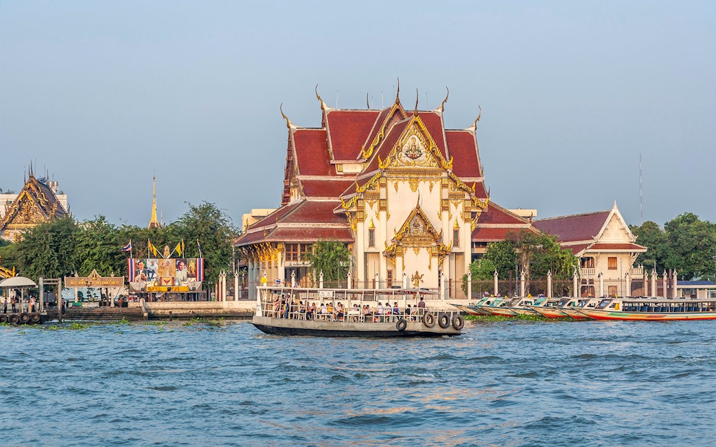 Boat on Chao Phraya River passing Wat Kalayanamit temple in Bangkok.