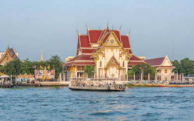 Boat on Chao Phraya River passing Wat Kalayanamit temple in Bangkok.