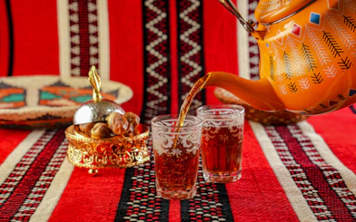 Traditional Omani tea being poured into ornate glasses on a patterned red cloth.