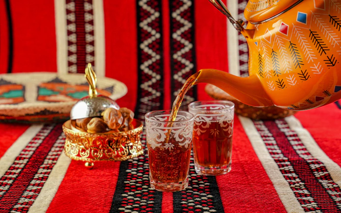 Traditional Omani tea being poured into ornate glasses on a patterned red cloth.