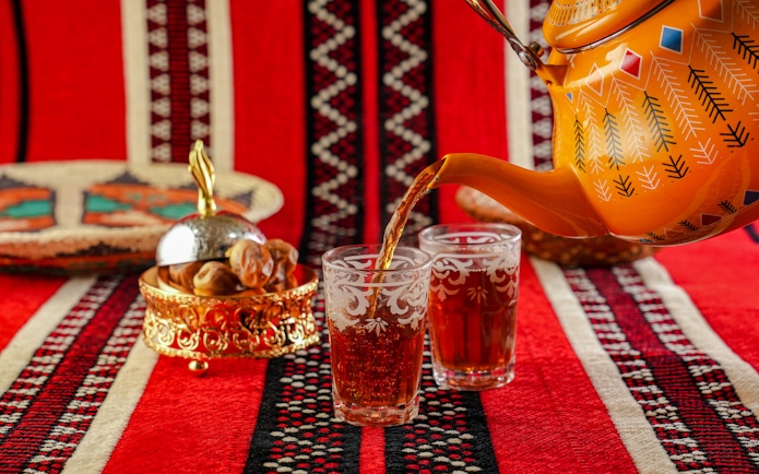 Traditional Omani tea being poured into ornate glasses on a patterned red cloth.