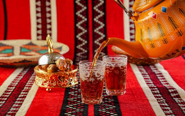 Traditional Omani tea being poured into ornate glasses on a patterned red cloth.