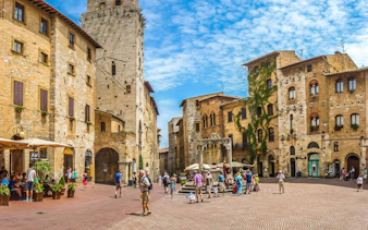 Piazza della Cisterna with tourists in San Gimignano, Italy, featuring medieval architecture.
