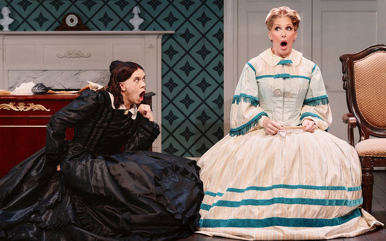Two women in period costumes express surprise during a theatrical performance of "Oh, Mary!