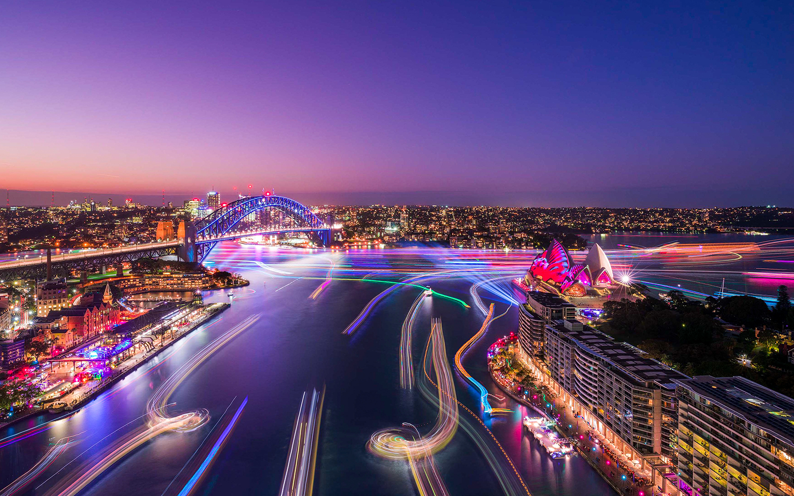 Aerial view of light trails from Vivid Sydney cruise ships near Sydney Harbour Bridge and Opera House.