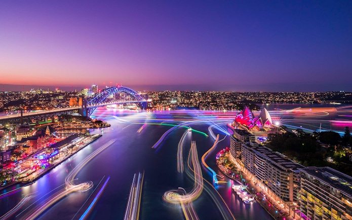 Aerial view of light trails from Vivid Sydney cruise ships near Sydney Harbour Bridge and Opera House.