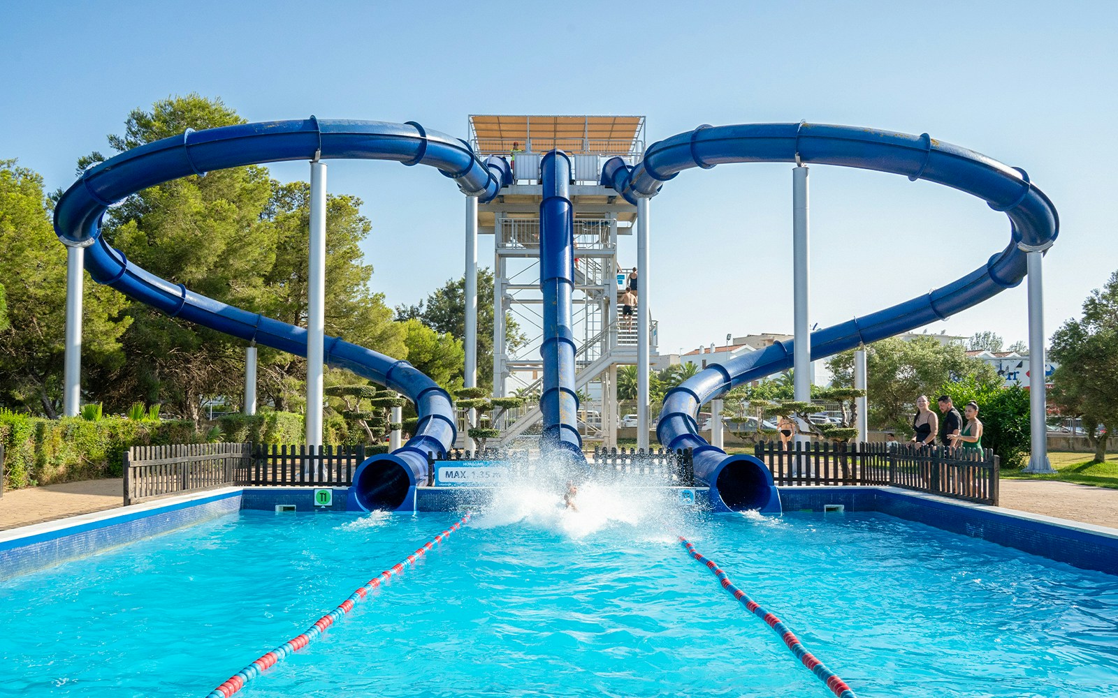 Water slide at Aquopolis Costa Dorada, Spain, with people enjoying the splash pool.