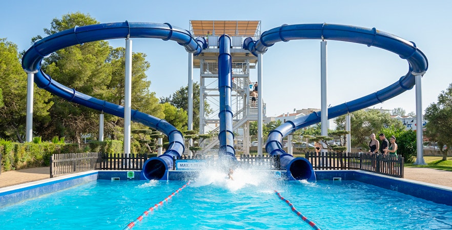 Water slide at Aquopolis Costa Dorada, Spain, with people enjoying the splash pool.