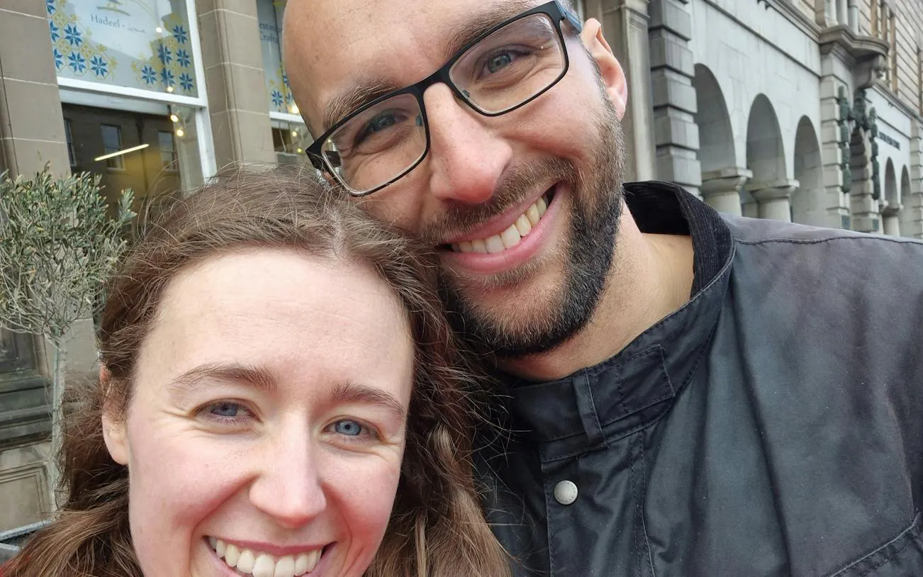 Couple smiling in front of historic Edinburgh building during city exploration game.