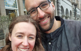 Couple smiling in front of historic Edinburgh building during city exploration game.