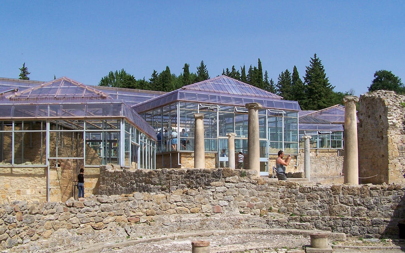 Villa Romana del Casale ruins with glass enclosures and visitors exploring.