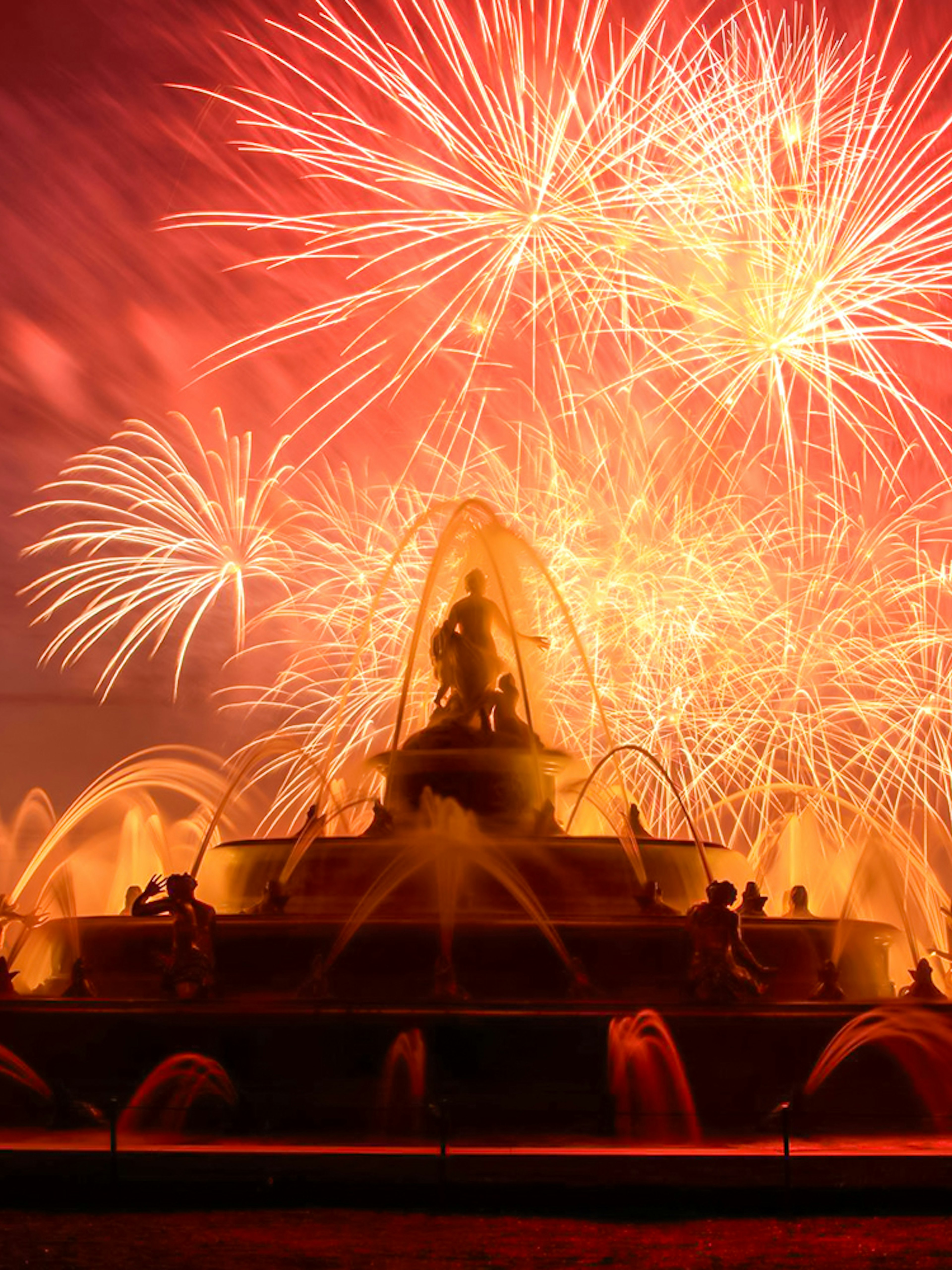 Versailles fountain illuminated by fireworks during night show from Paris.