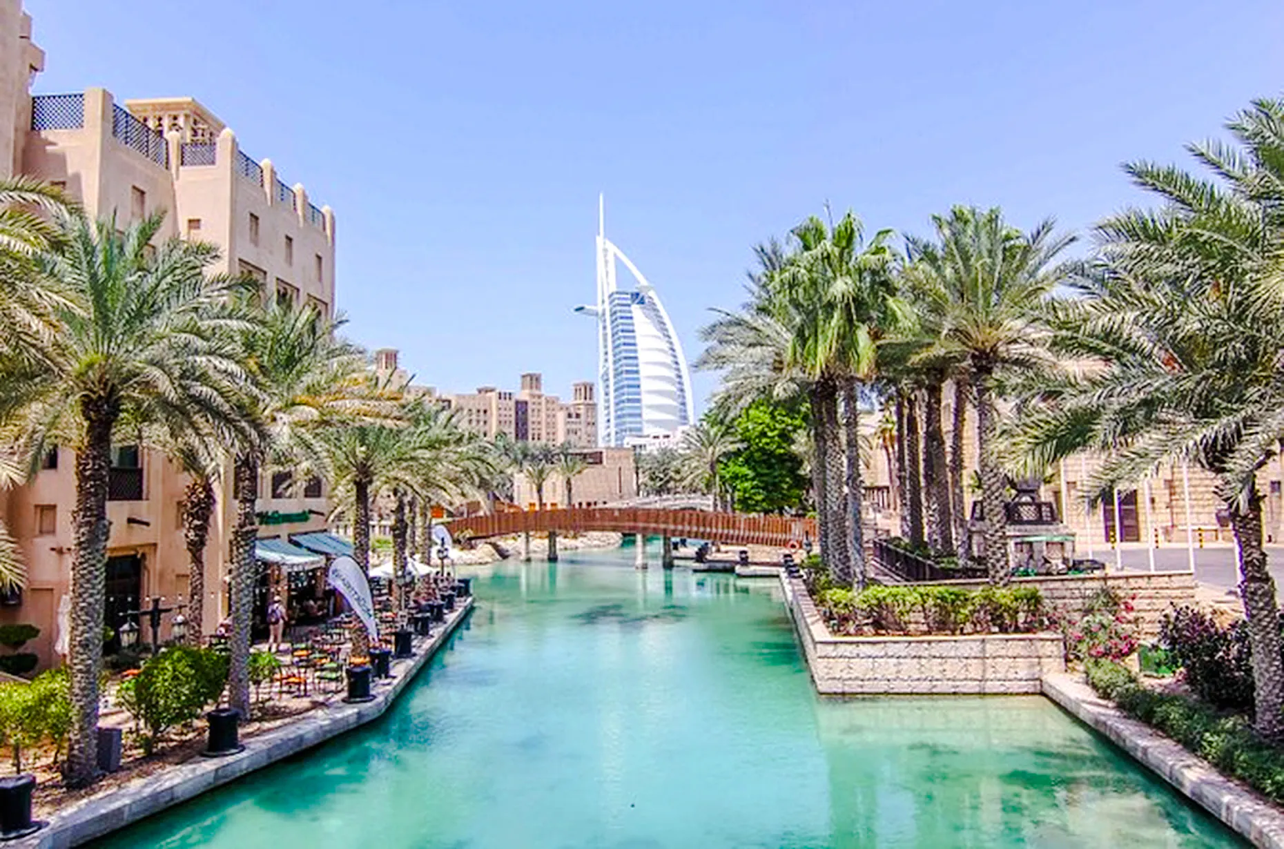 Dubai canal view with Burj Al Arab in the background, palm trees lining the waterway.