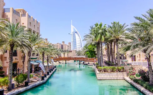 Dubai canal view with Burj Al Arab in the background, palm trees lining the waterway.