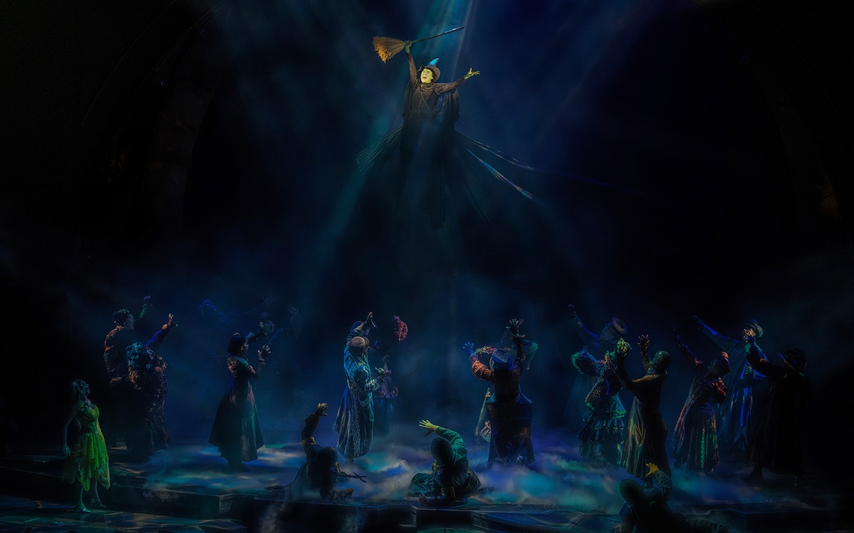 Stage scene from the musical Wicked with characters in dramatic lighting.