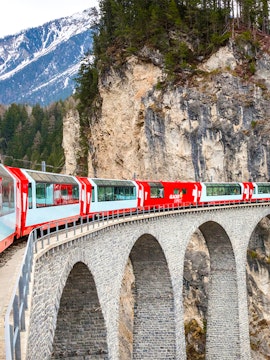 Glacier Express train crossing a stone viaduct in the Swiss Alps.