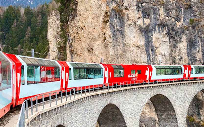 Glacier Express train crossing a stone viaduct in the Swiss Alps.