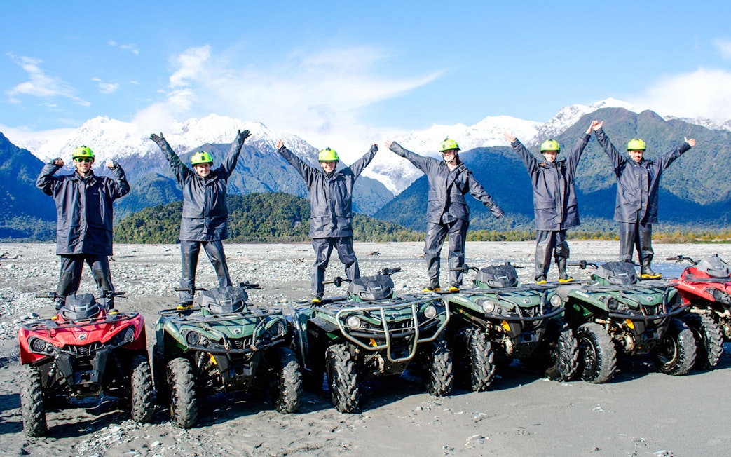 Group standing on quad bikes with arms raised, Franz Josef, New Zealand.