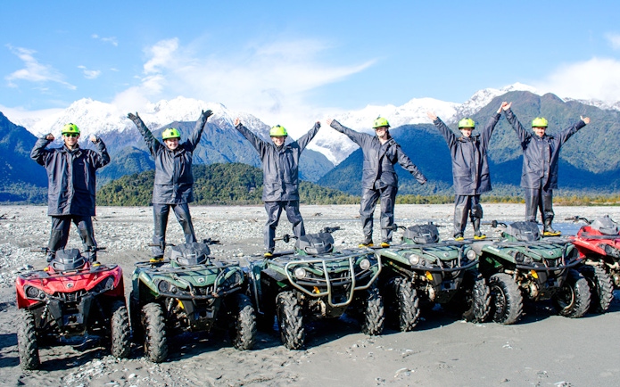 Group standing on quad bikes with arms raised, Franz Josef, New Zealand.