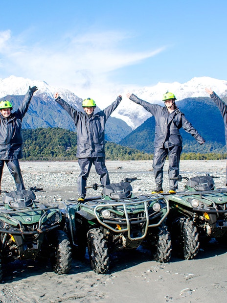Group standing on quad bikes with arms raised, Franz Josef, New Zealand.