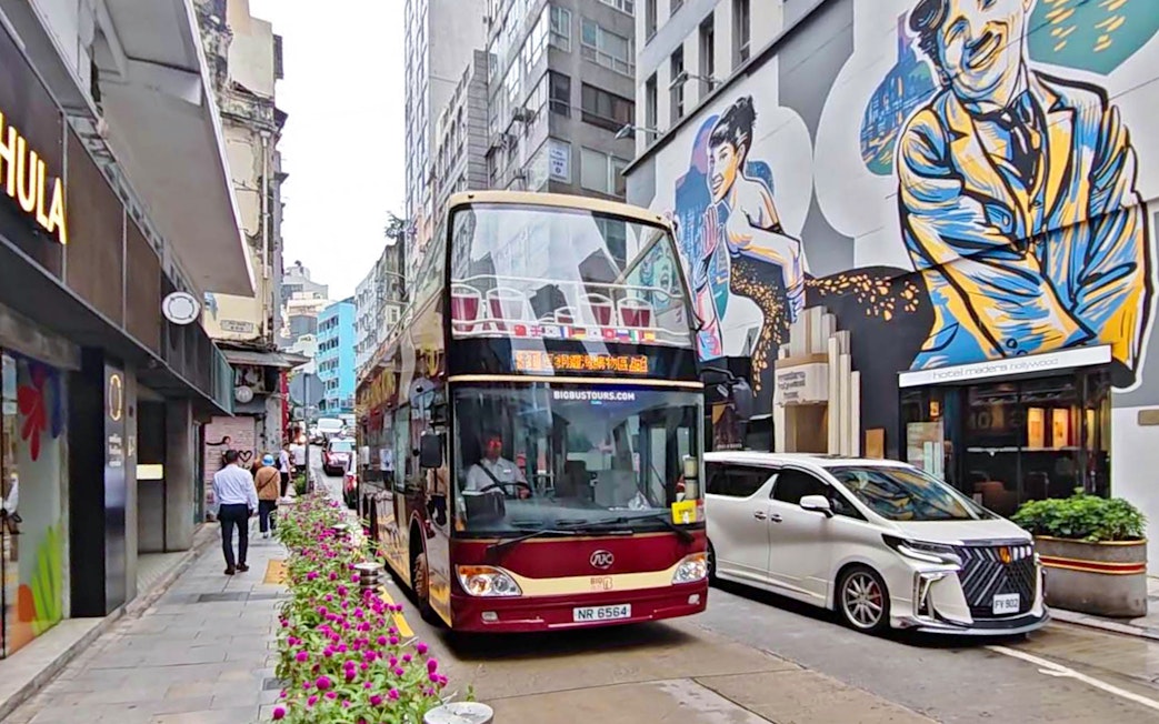 Double-decker bus on Hong Kong street with colorful mural, part of Big Bus Tour.