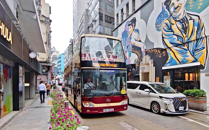 Double-decker bus on Hong Kong street with colorful mural, part of Big Bus Tour.