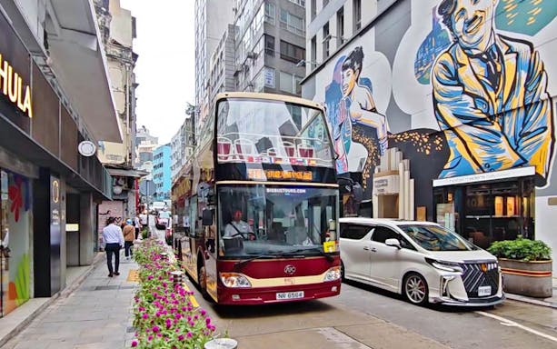 Double-decker bus on Hong Kong street with colorful mural, part of Big Bus Tour.