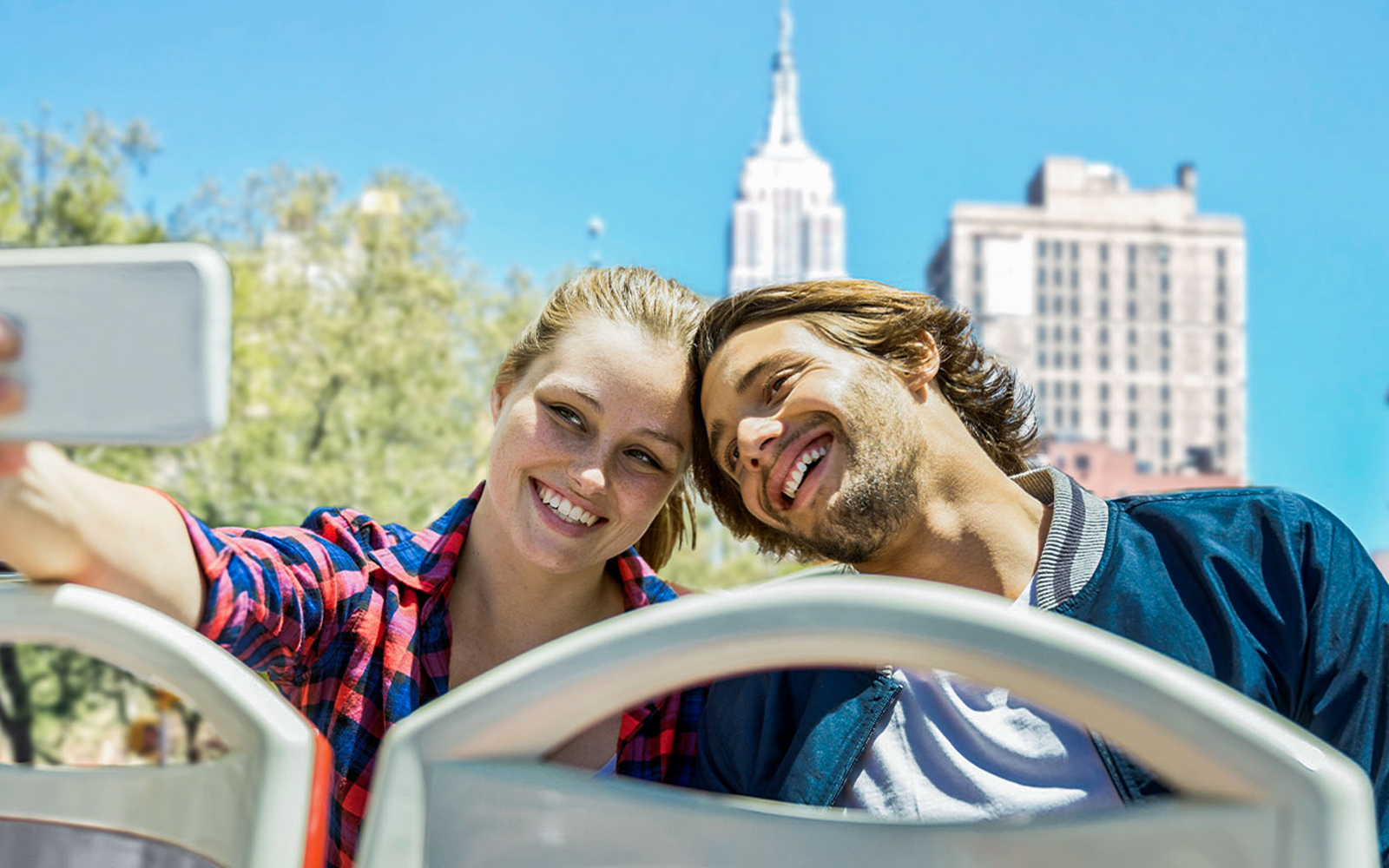 Couple taking selfie on New York Hop On Hop Off bus with Empire State Building.