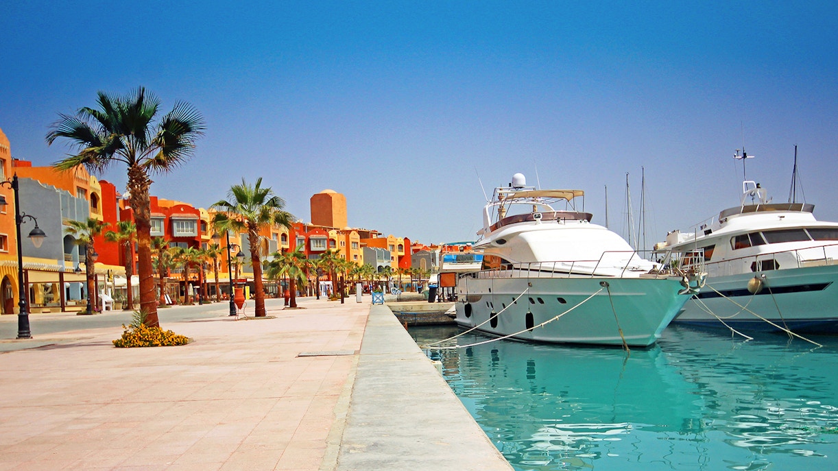 Yachts docked at Hurghada Marina with colorful buildings and palm trees along the Corniche.