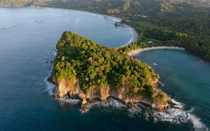 Aerial view of Manuel Antonio National Park coastline at sunrise, featuring lush greenery and ocean.