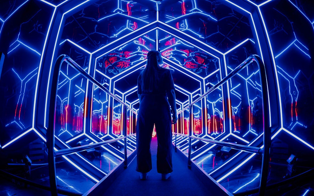 Visitor exploring neon-lit tunnel at Amaze Amsterdam.