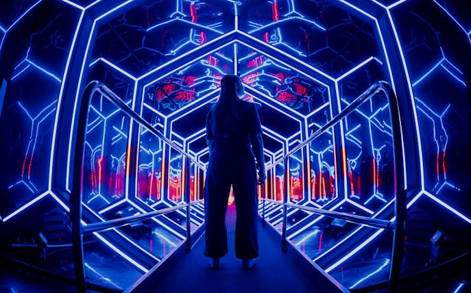 Visitor exploring neon-lit tunnel at Amaze Amsterdam.