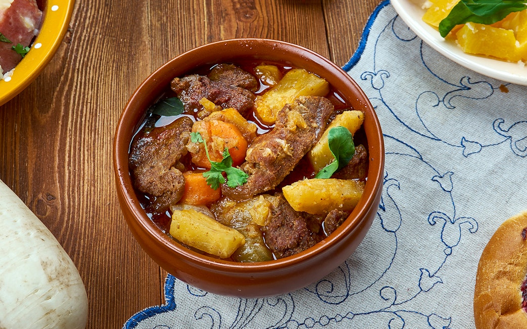 Sami stew with meat, potatoes, and carrots in a brown bowl on a wooden table.