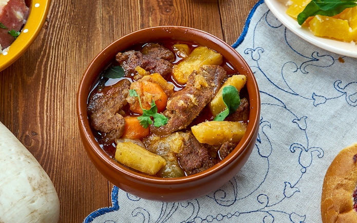 Sami stew with meat, potatoes, and carrots in a brown bowl on a wooden table.