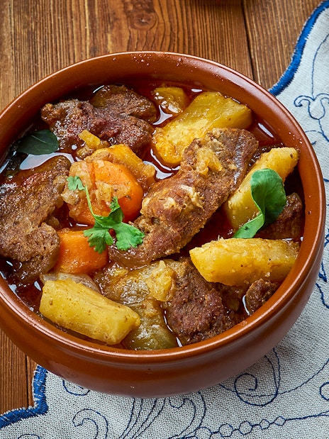 Sami stew with meat, potatoes, and carrots in a brown bowl on a wooden table.