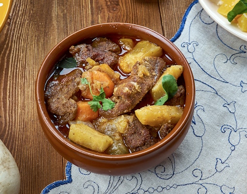 Sami stew with meat, potatoes, and carrots in a brown bowl on a wooden table.