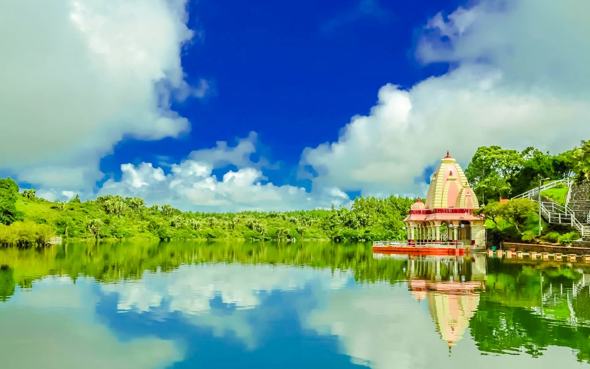 Hindu temple by the lake at Ganga Talao, Mauritius, with lush greenery and blue sky.