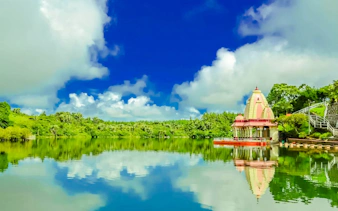 Hindu temple by the lake at Ganga Talao, Mauritius, with lush greenery and blue sky.
