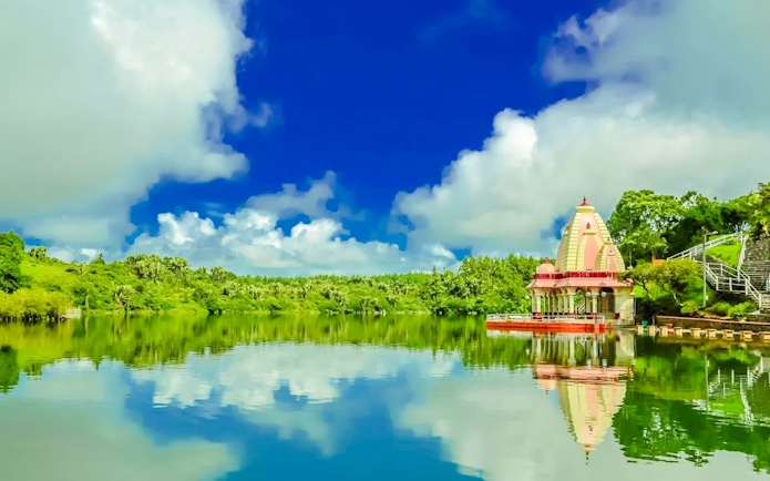 Hindu temple by the lake at Ganga Talao, Mauritius, with lush greenery and blue sky.