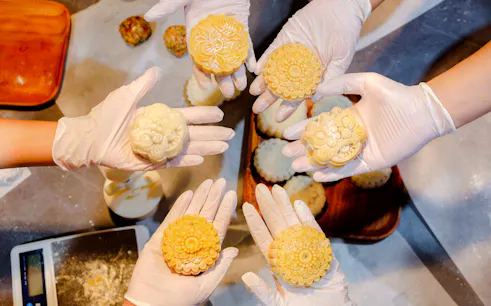 Gloved hands holding baked and snow skin mooncakes during a workshop in Hanoi.
