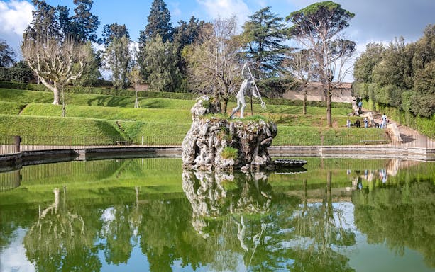 Sculpture in Boboli Gardens, Florence, reflected in a pond with surrounding greenery.