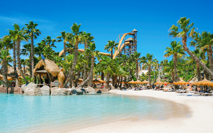 Caribe Bay beach with palm trees, water slides, and sunbathers on loungers.
